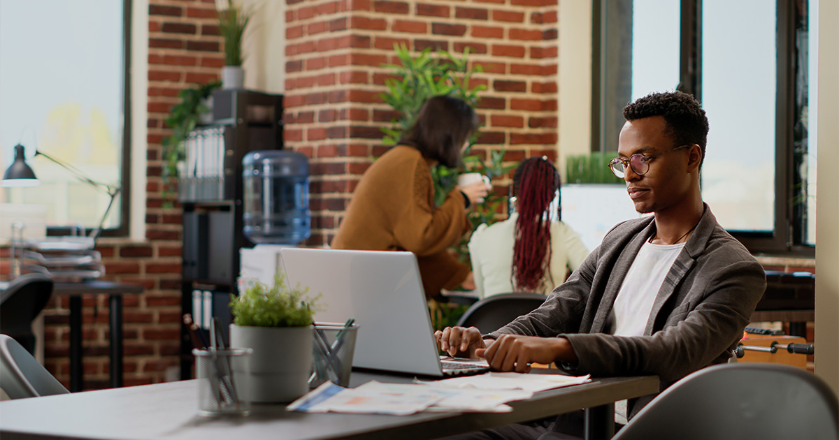 A person in an office setting is working on their laptop. They are researching cannabis market data to maximize their ROI as discussed in CannaSpyglass's e-book 'The smarter way to research cannabis market data'.